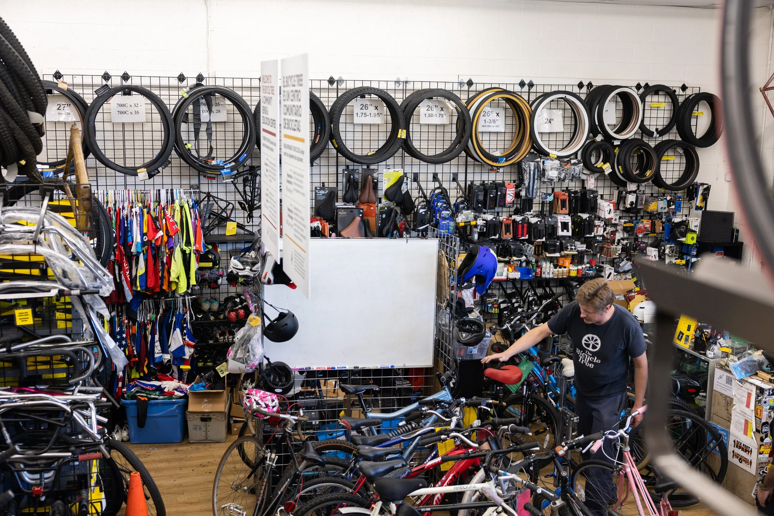 A community member shopping for bicycles inside a bike shop, surrounded by various bikes, tires, helmets, and cycling accessories on display.