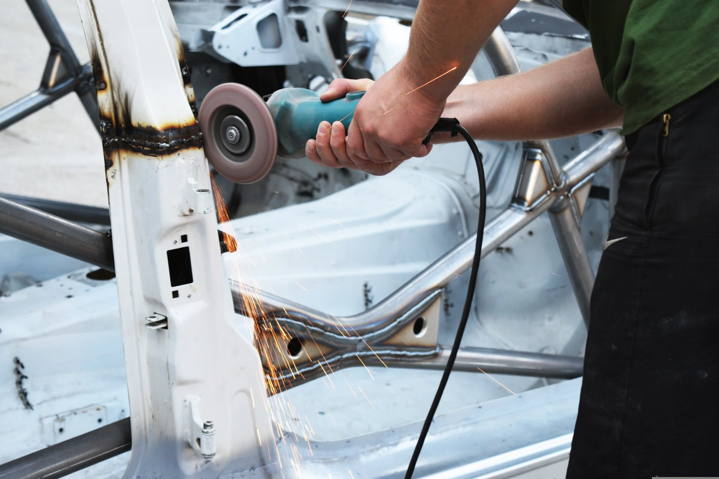 Person using a handheld angle grinder to cut or grind metal on a vehicle frame, with sparks flying, in an automotive workshop.