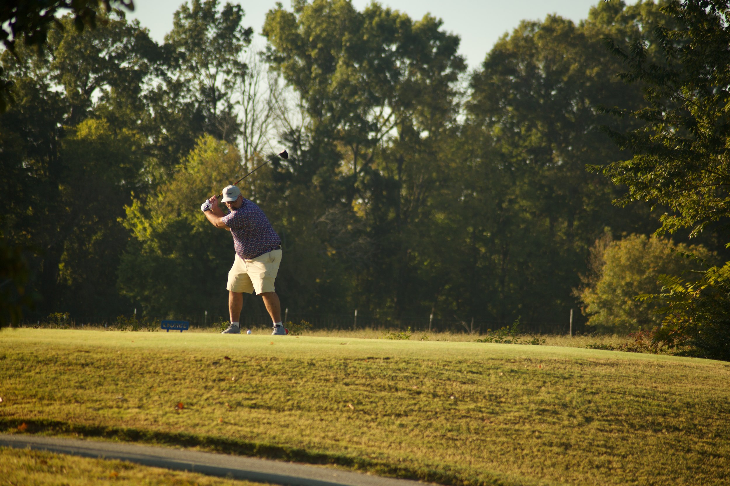 A man golfing on a golf course during daytime, preparing to swing a golf club with trees in the background.