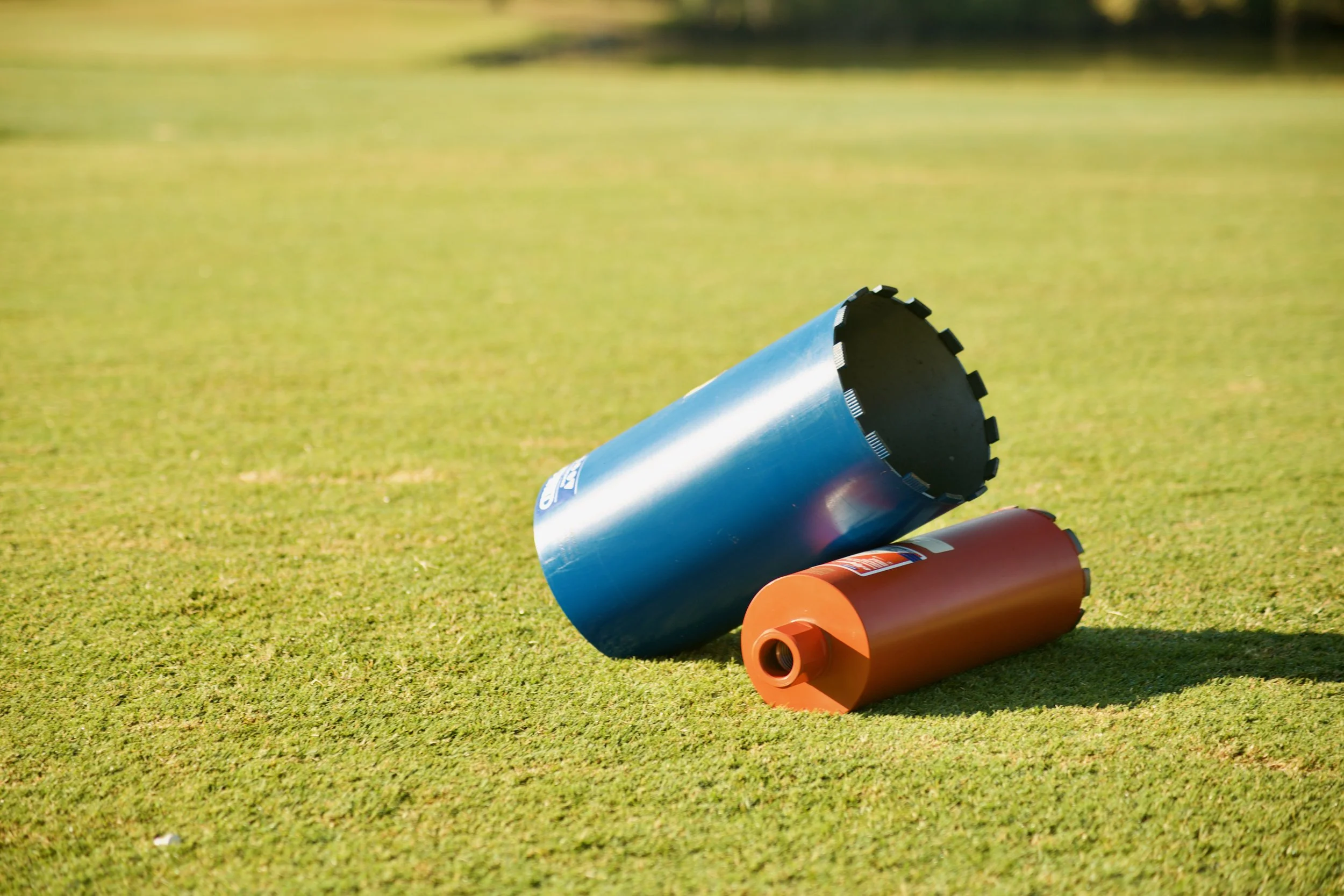 Three colorful lawn rollers resting on a green grassy field with blurred trees in the background.
