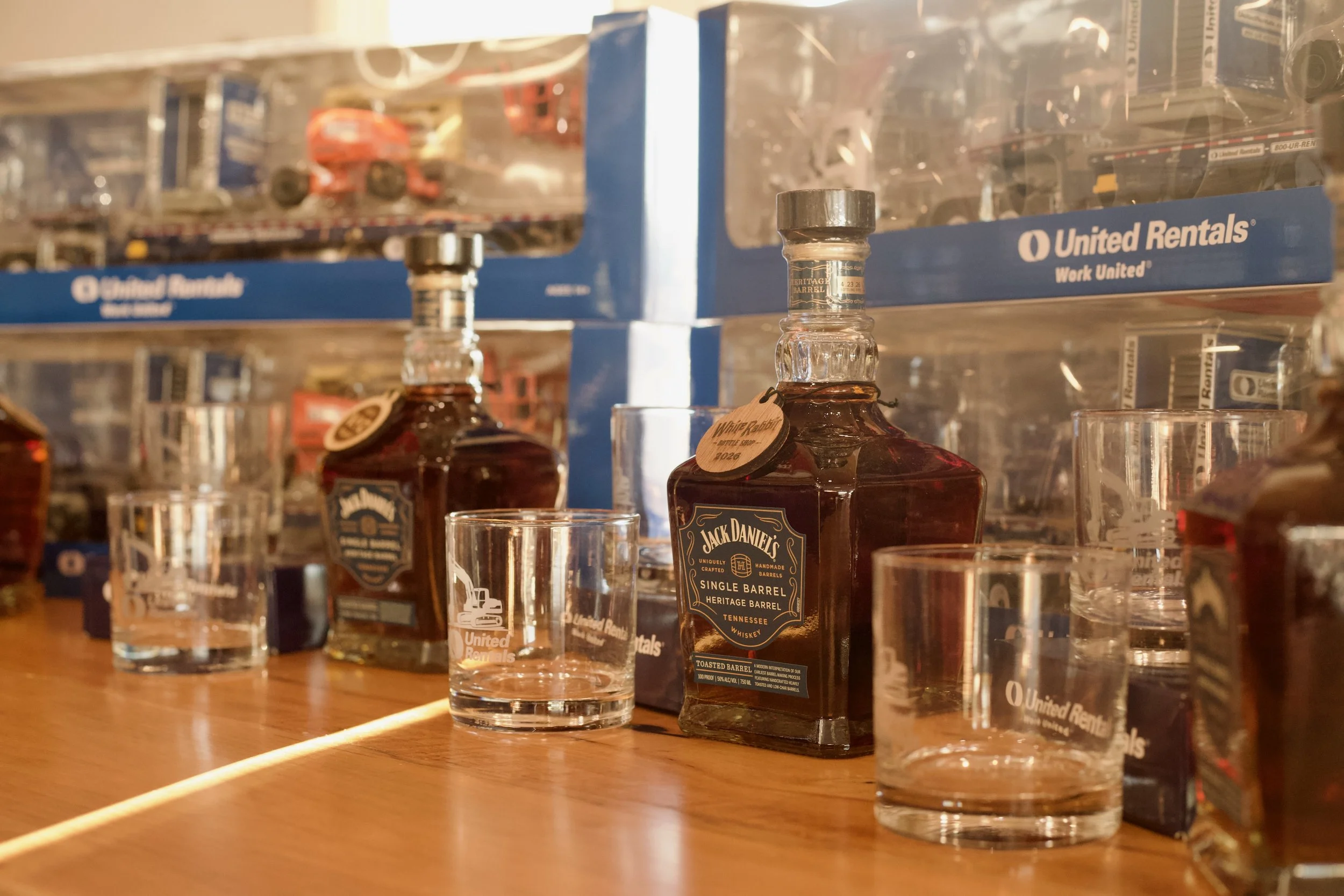 Bar shelf with whiskey bottles, empty glasses, and plastic storage boxes from United Rentals.