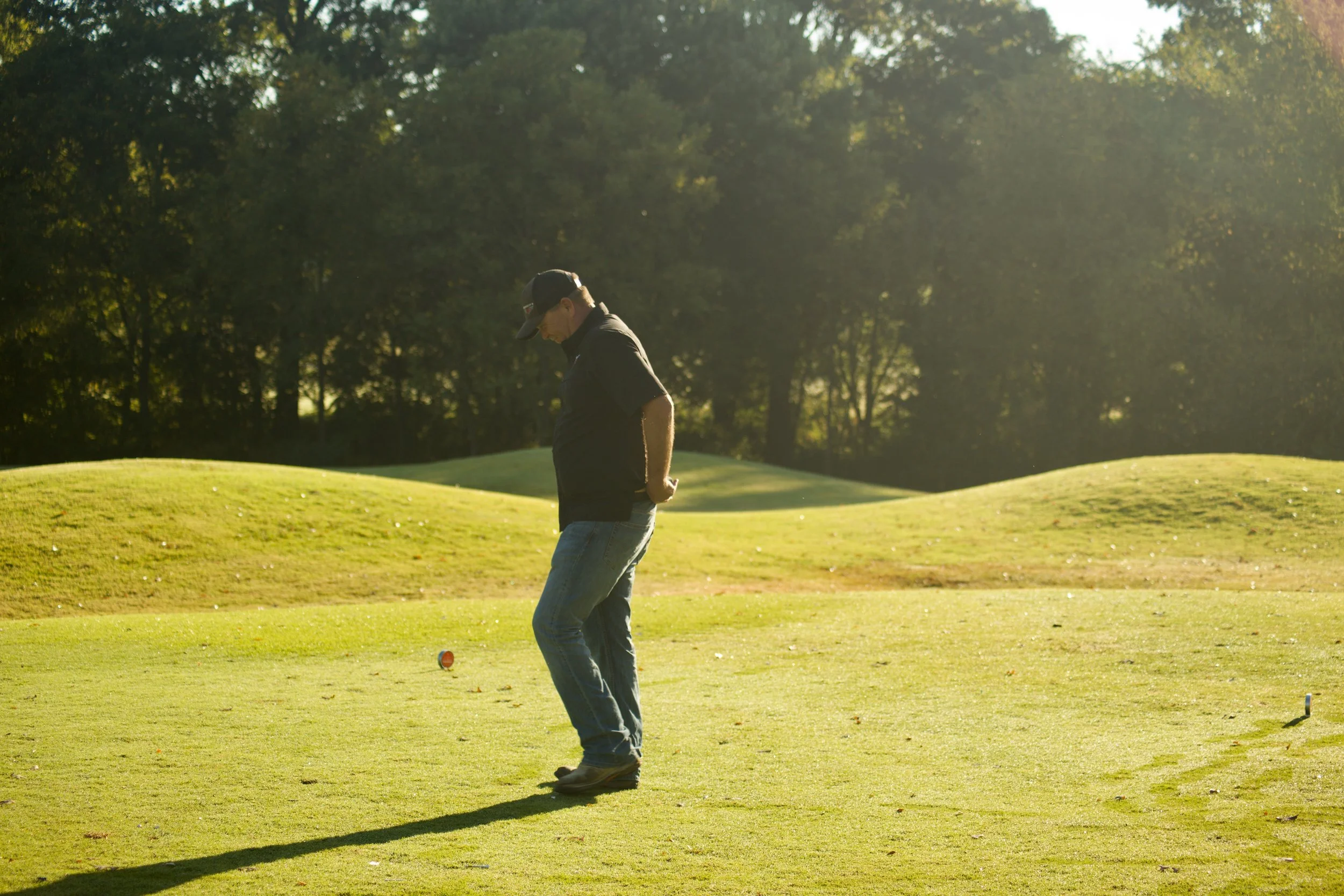 A person standing on a golf course, preparing to hit a golf ball with a club during sunset.