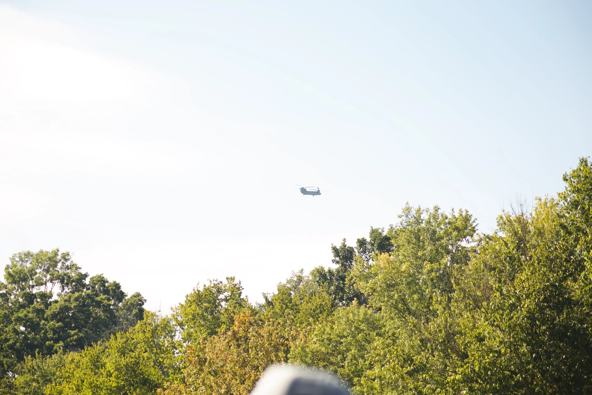 A helicopter flying in the sky above green trees with a clear bright sky