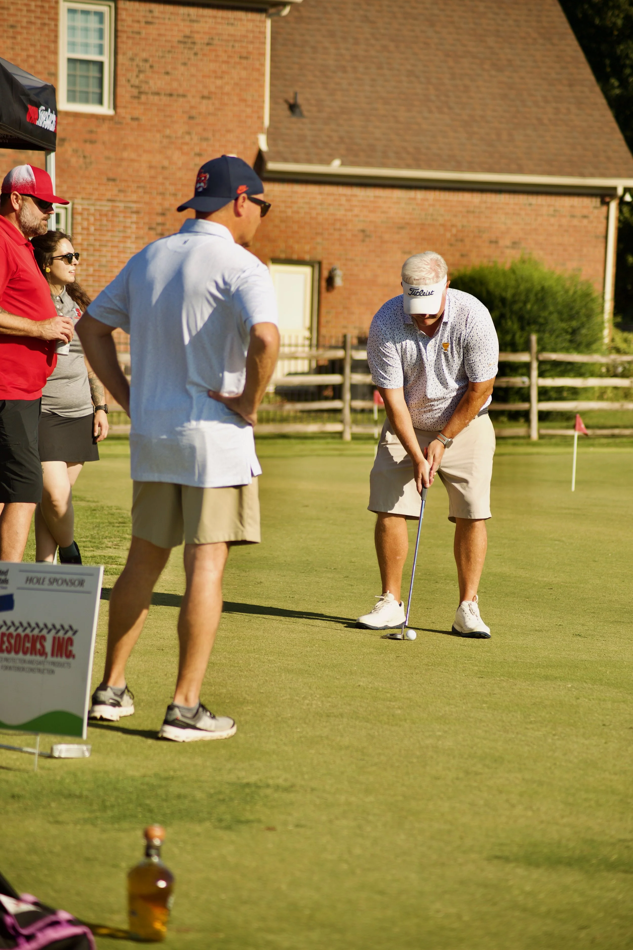 Man practicing putting golf on green, surrounded by spectators under sunny sky.