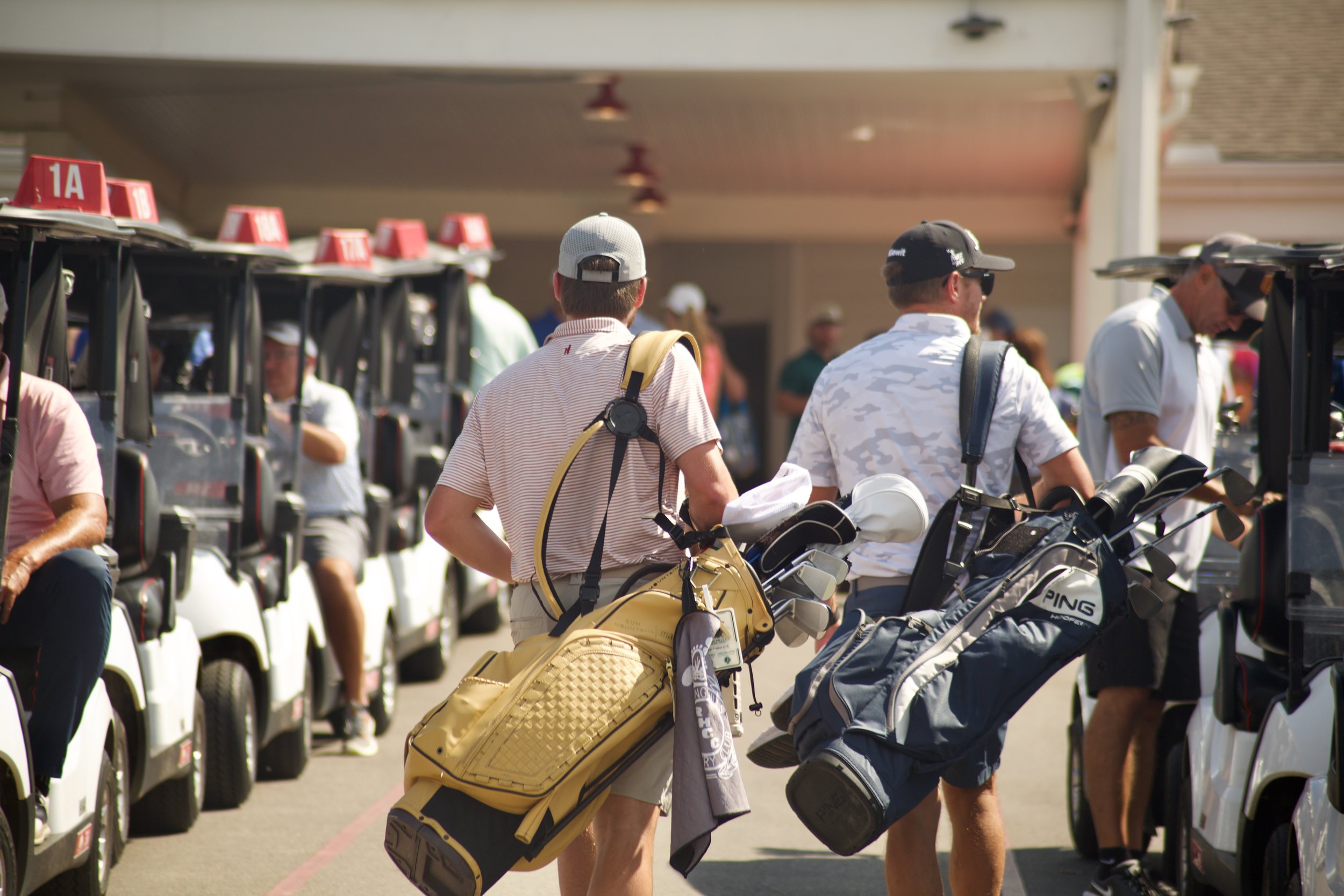 People at a golf course, loading golf clubs onto golf carts.
