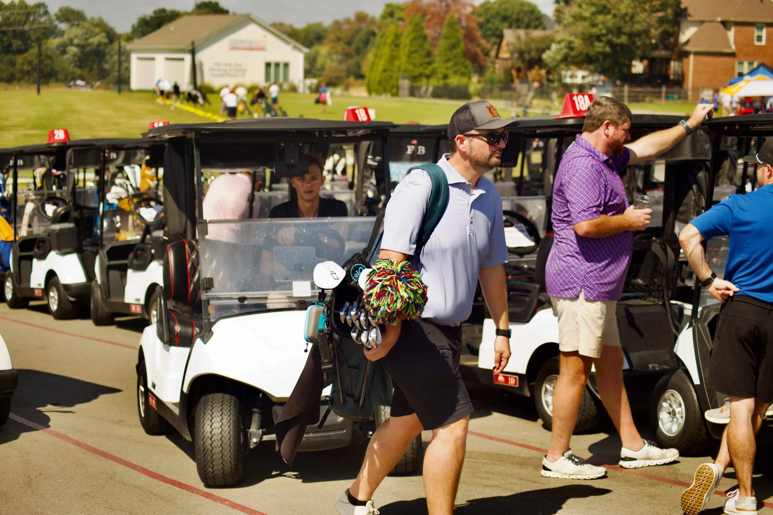 People walking past golf carts at a golf course during a sunny day.