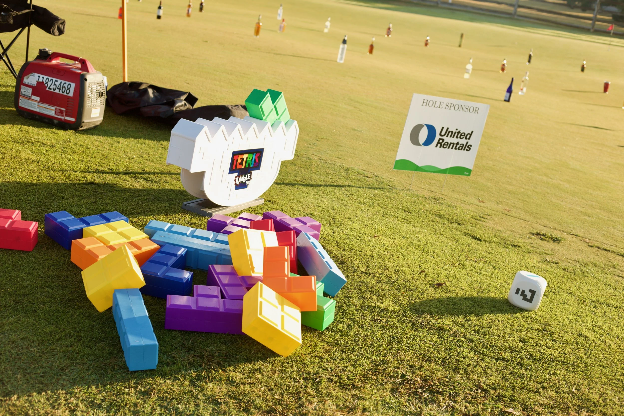 Colorful Tetris-themed mini-golf course with scattered game pieces, a logo sign, and sponsorship signs on a grassy field.