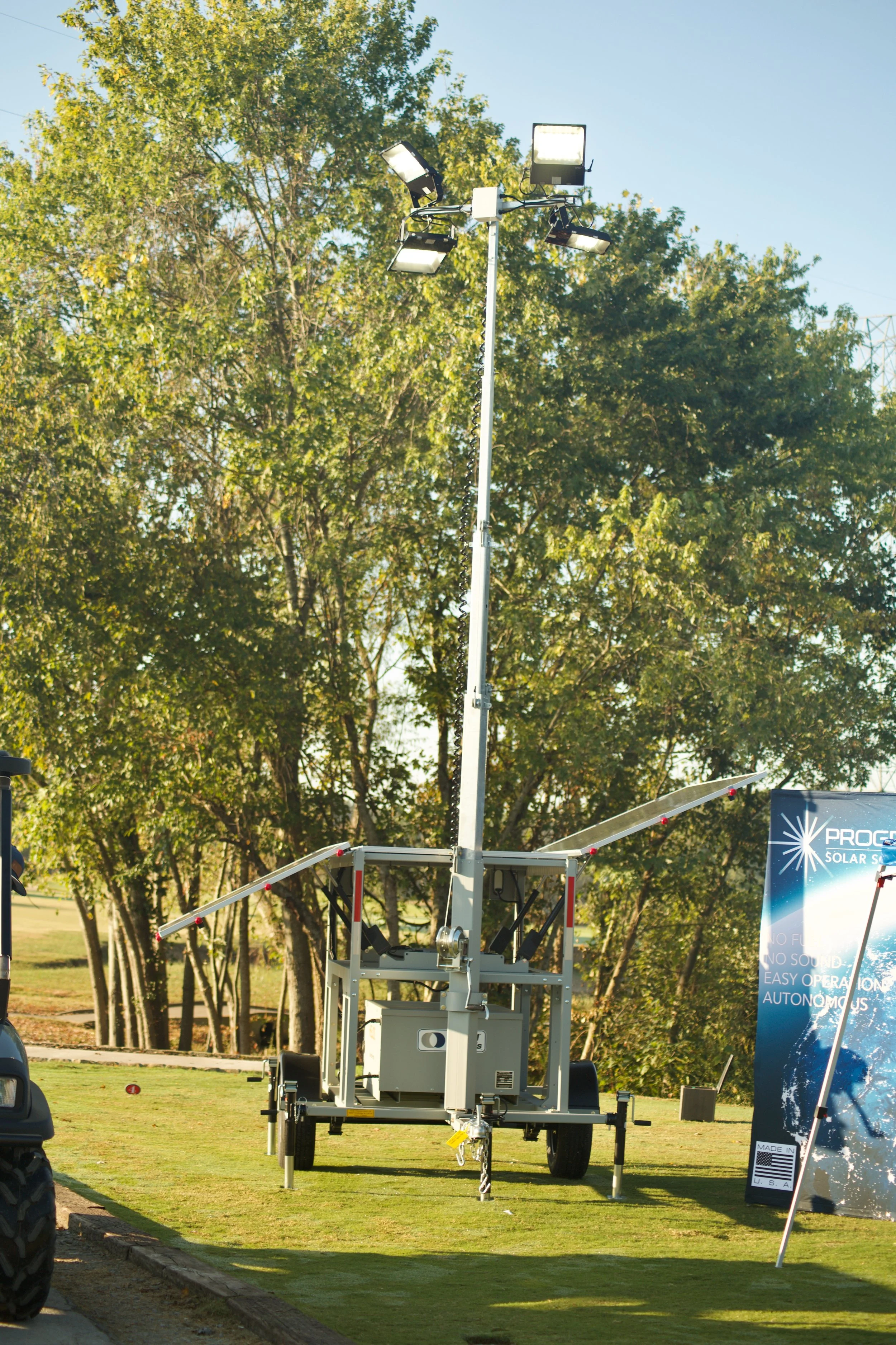 A large outdoor machine with several bright lights mounted on top, situated in a park or open field with trees in the background.