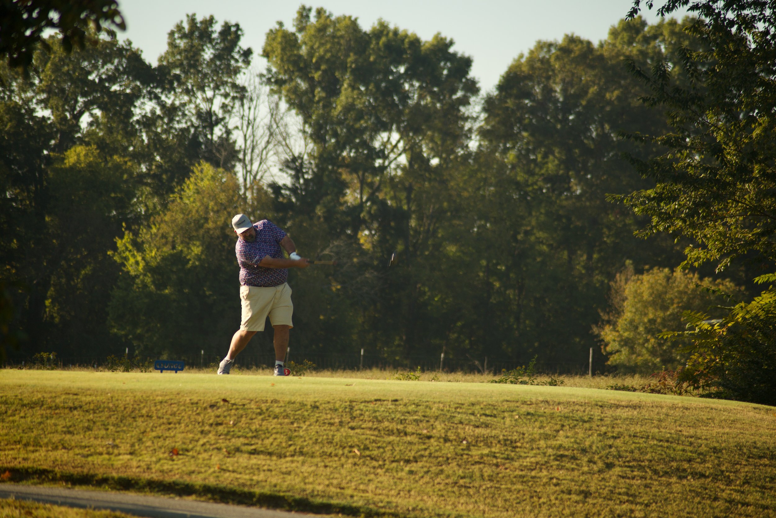 A man playing golf on a course surrounded by trees during the day.