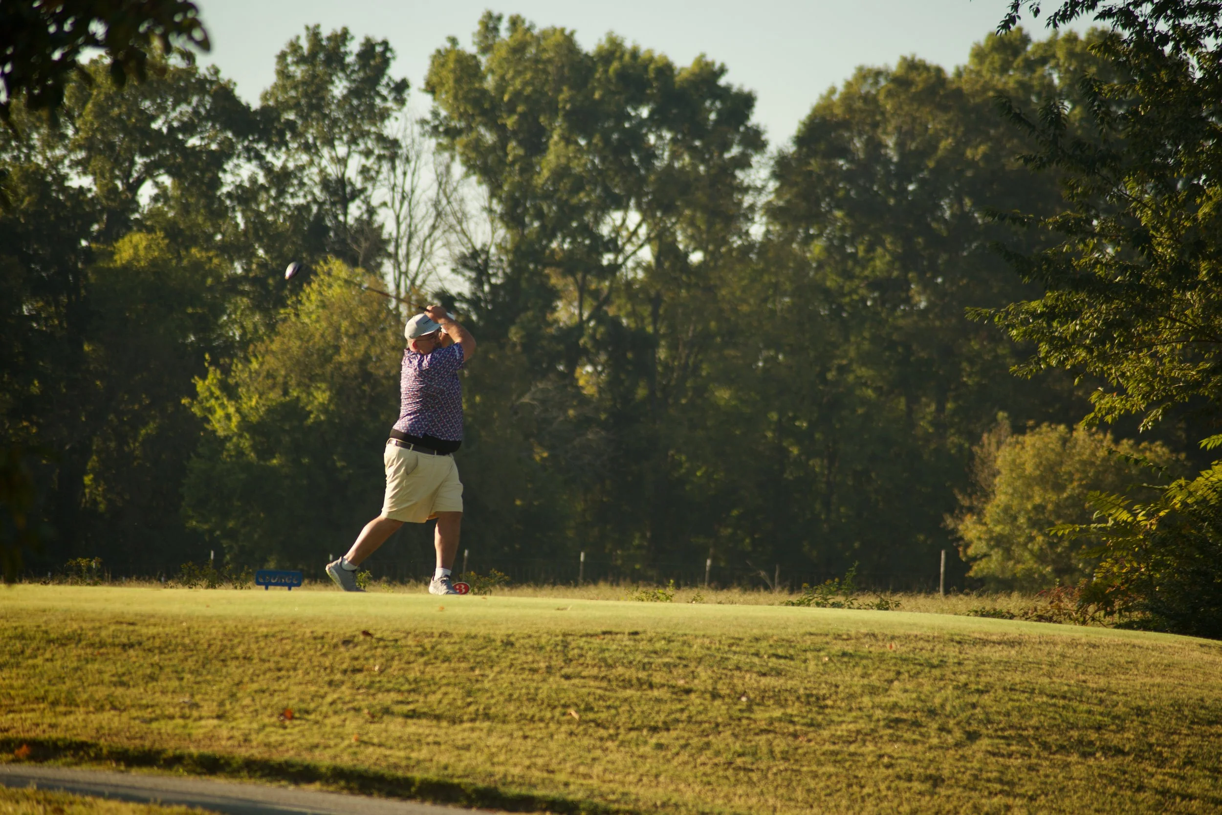 A man playing golf on a golf course with lush green grass and tall trees in the background
