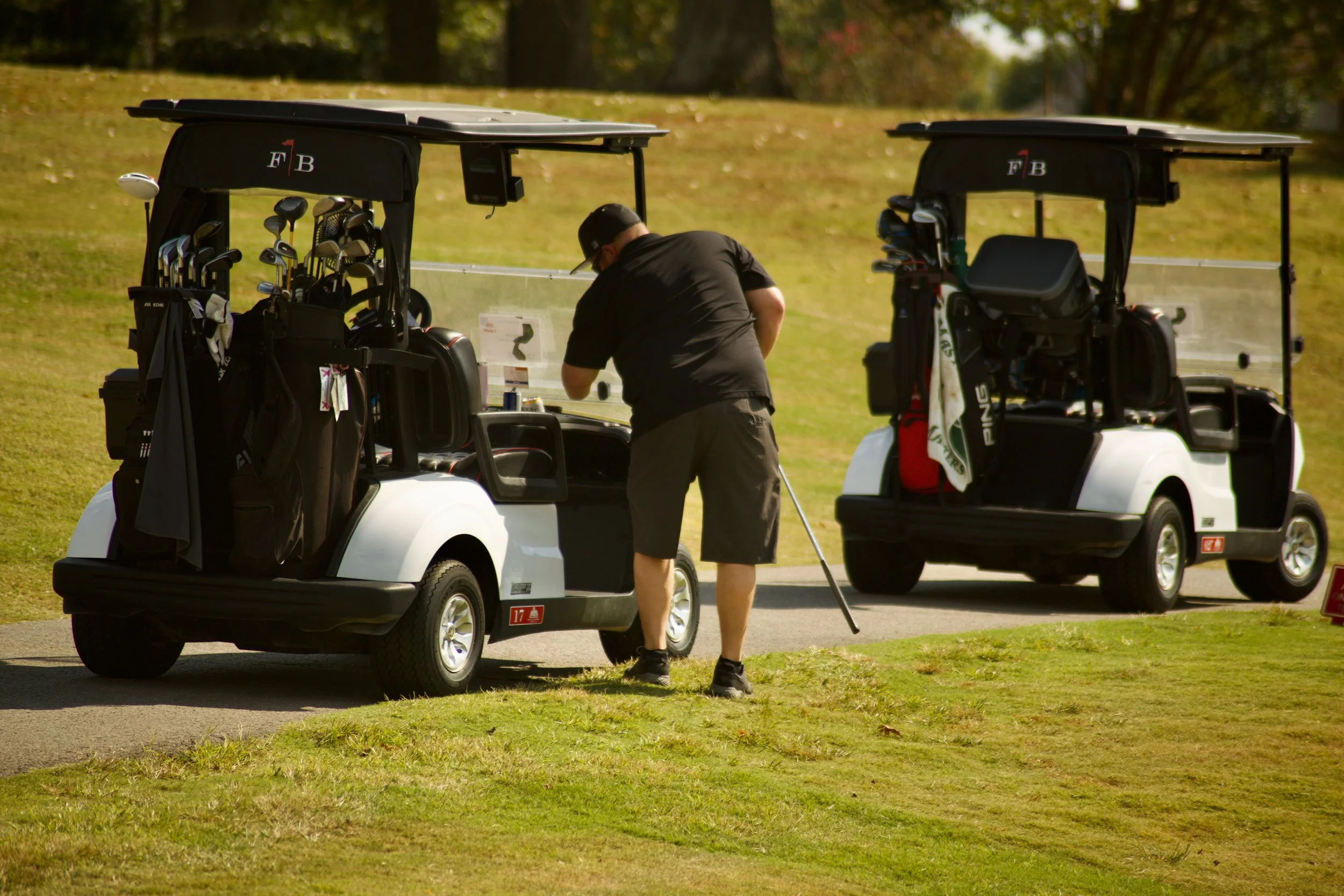 A man adjusting golf clubs in a golf cart on a golf course with trees and grass in the background.