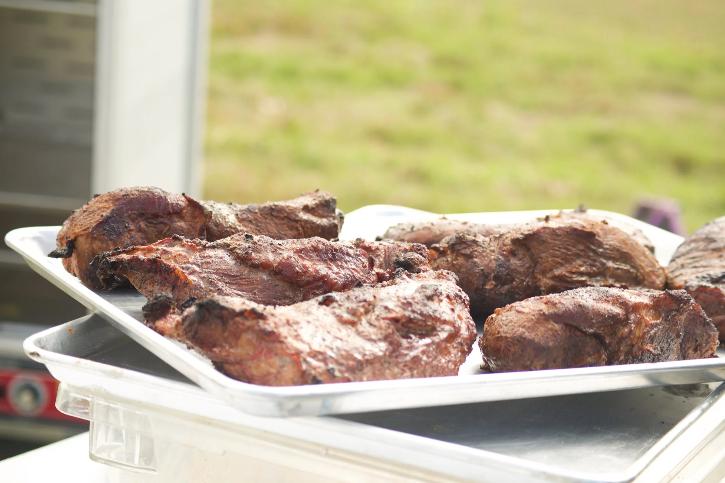 Close-up of grilled meat steaks on a white plastic tray outdoors on a sunny day.