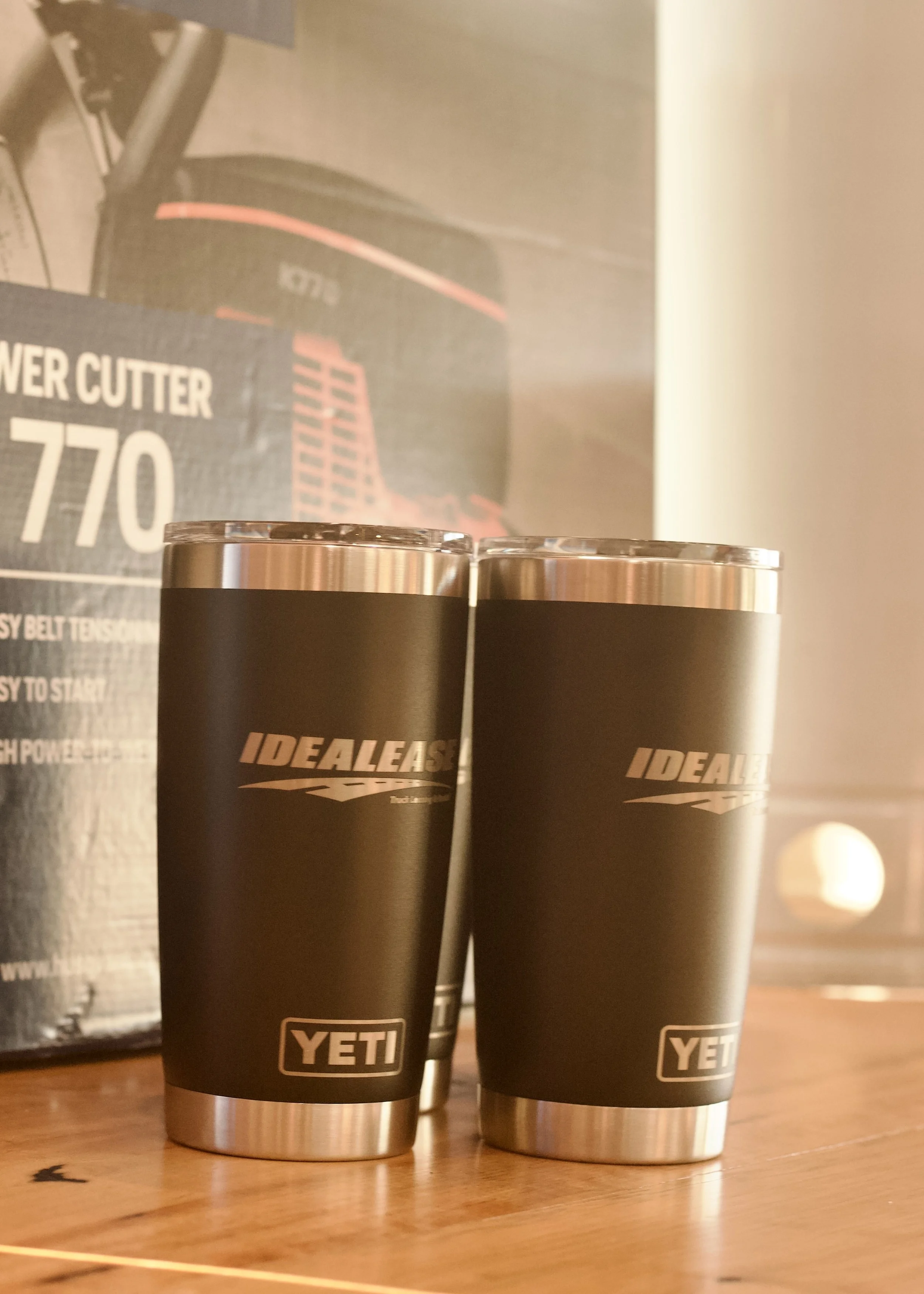 Two black YETI insulated tumblers with silver tops sitting on a wooden surface, with a YETI Power Cutter box and a dark-colored box in the background.