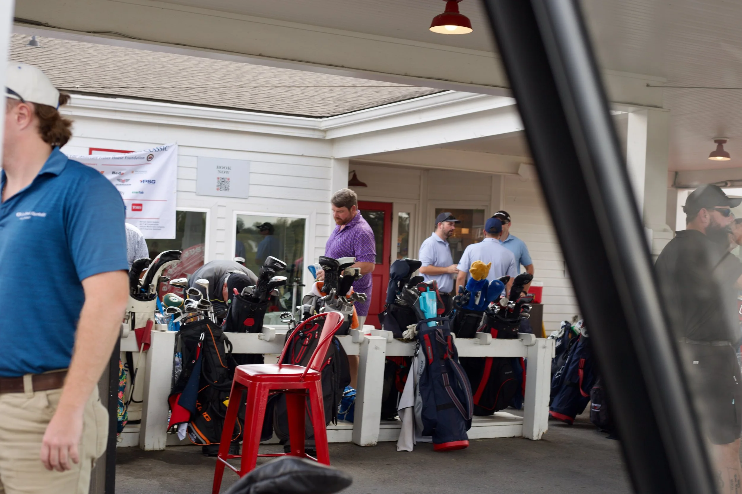 People at a golf equipment display with golf bags and clubs outside of a building.