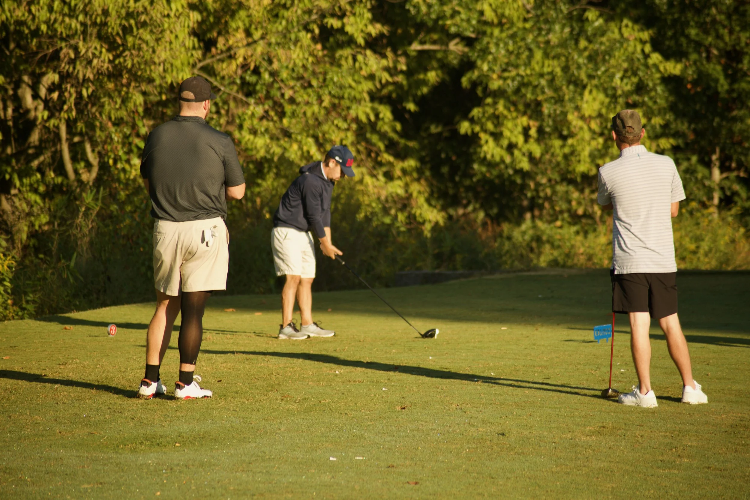 Group of four people playing golf on a green course near trees, with two men and two women, some preparing to putt.