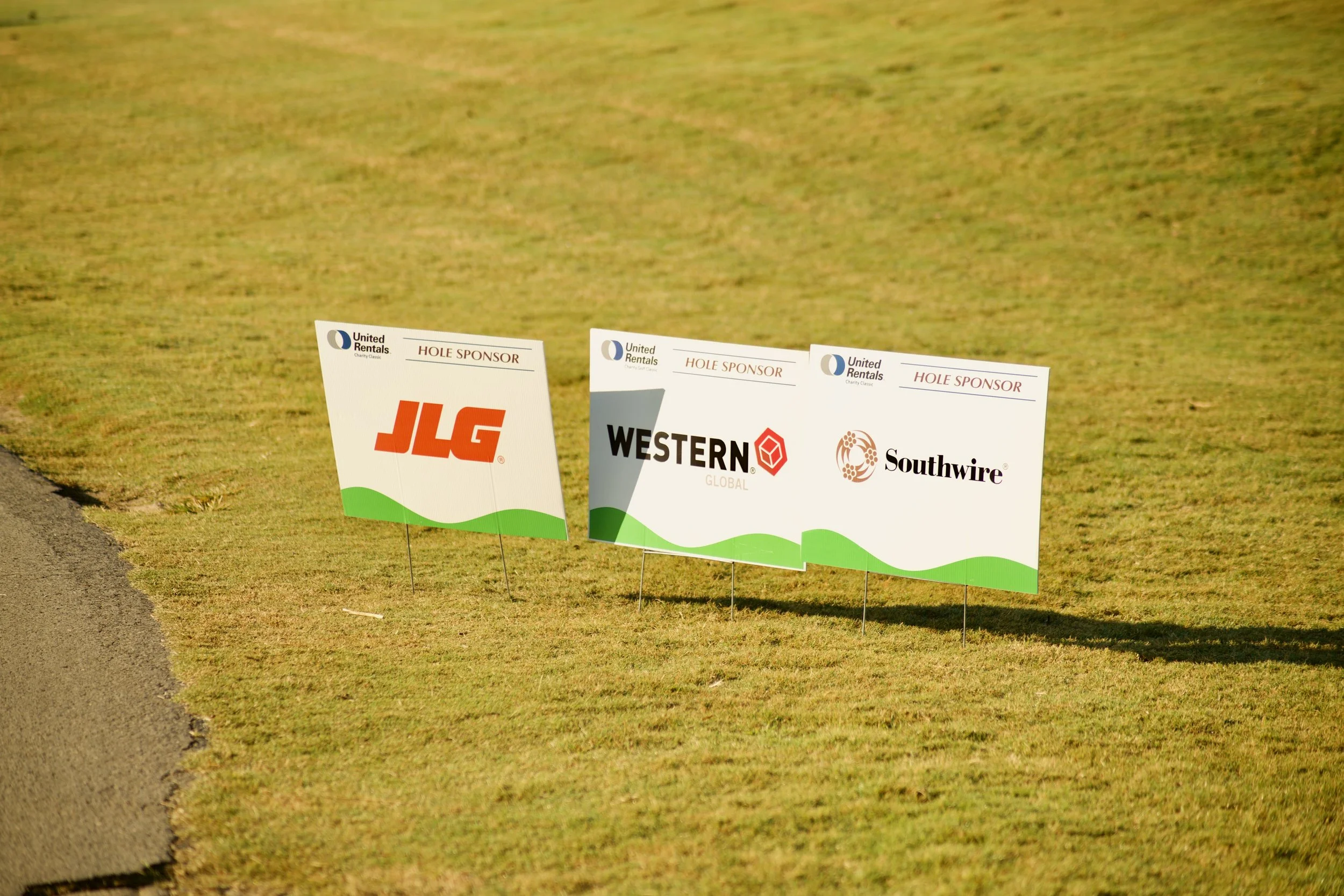 Golf course with sponsor signs for JLG, Western Global, and Southwire along the grassy edge next to the green.