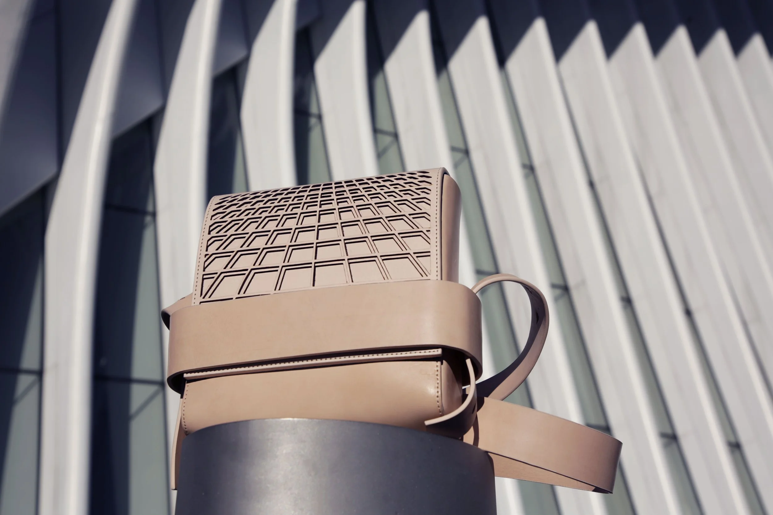 Beige leather handbag with geometric pattern on cylindrical pedestal, modern architectural background