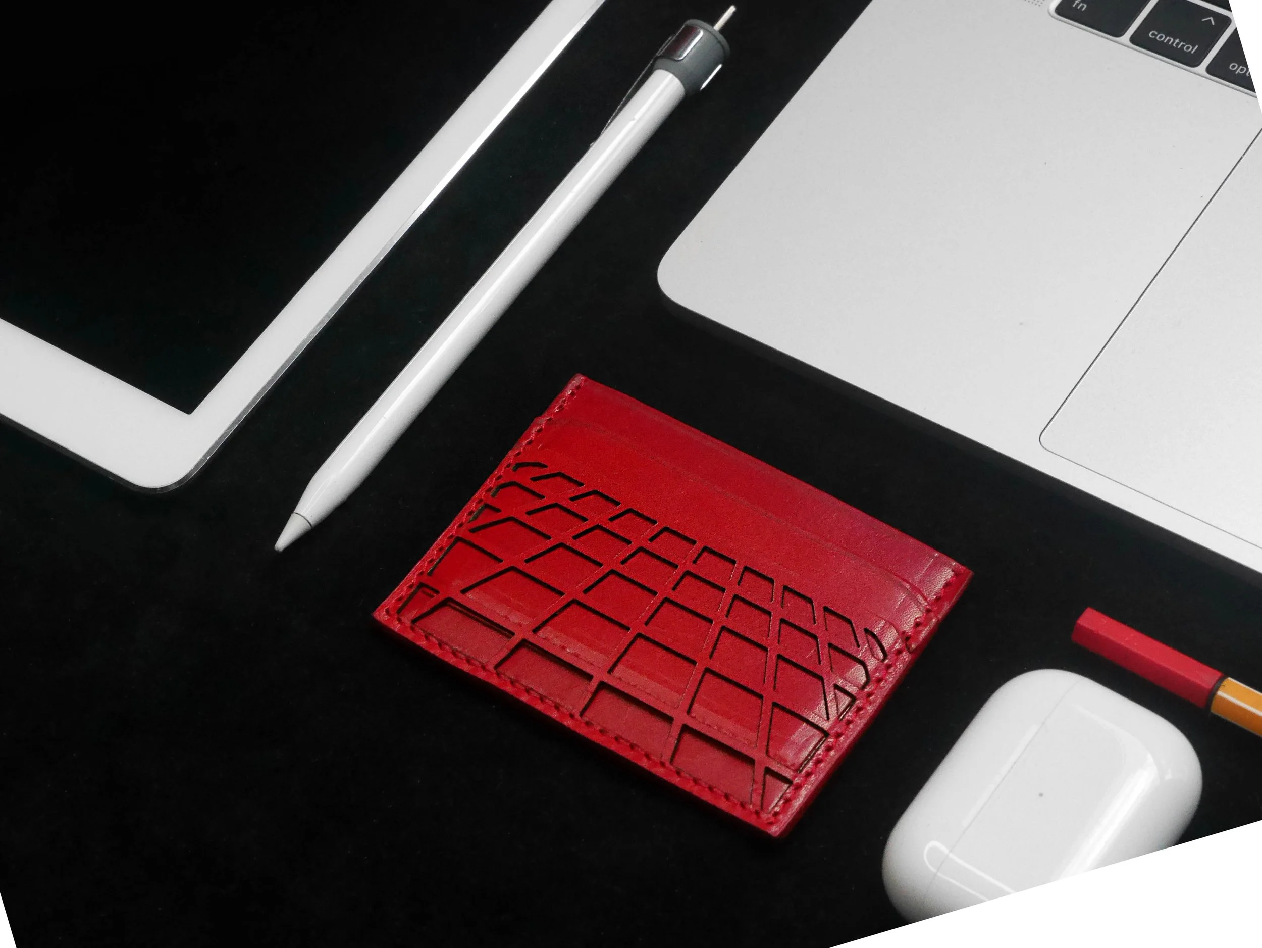 Desk with tablet, laptop, stylus, red wallet, AirPods, and colored pencil.