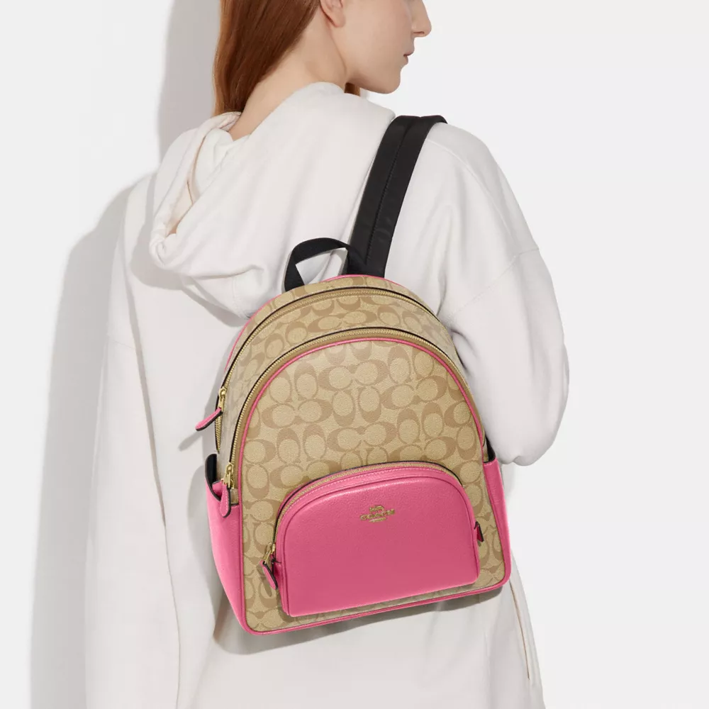 Person wearing a white hoodie with a tan and pink designer Coach backpack featuring a signature pattern.