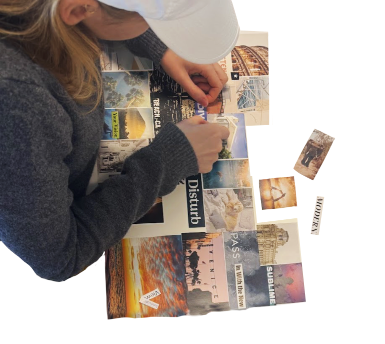 A person wearing a white cap and gray sweater is arranging travel photos and postcards on a table, which also features a large poster with various images and text.