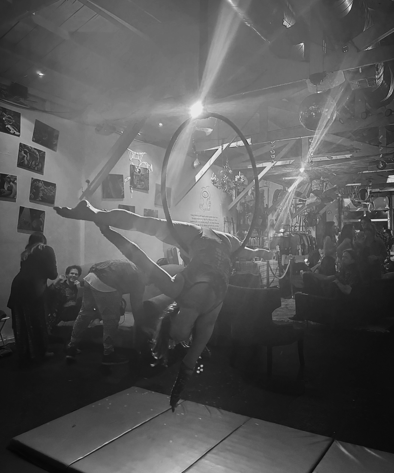Aerialist performing on an aerial hoop in a dimly lit room, with people watching and taking photos.