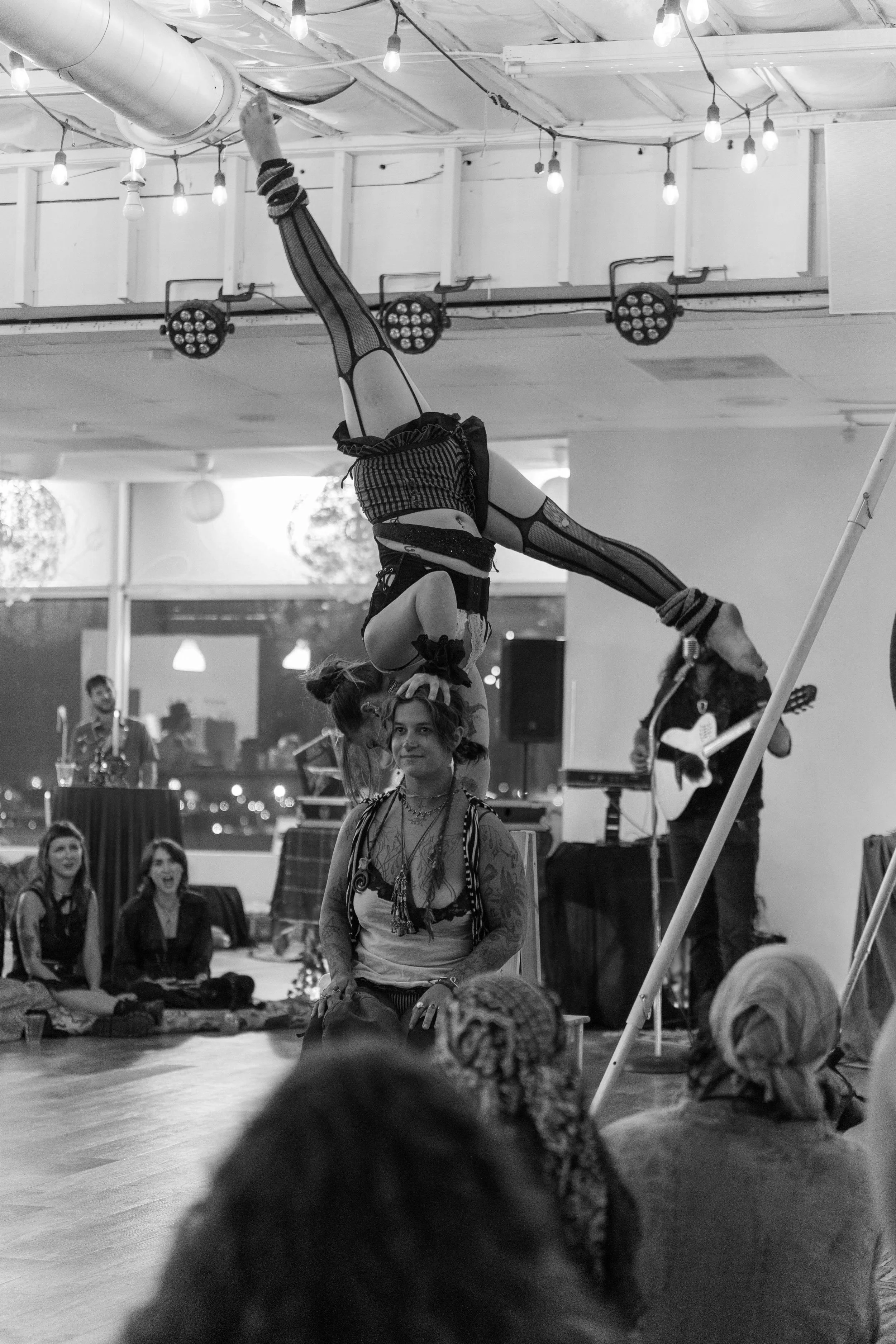 A performer doing a handstand on another person's head during a circus or acrobatic act in an indoor setting, with an audience watching.