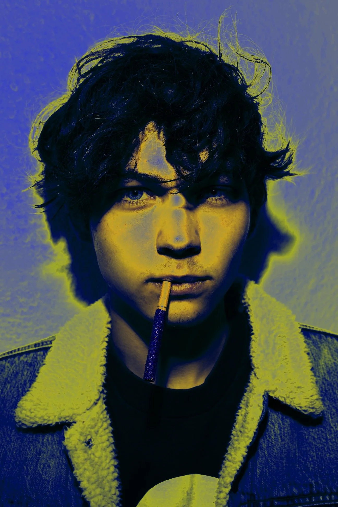 A young man with curly hair holding a cigarette in his mouth, wearing a jacket with a fuzzy collar, looking intensely at the camera.
