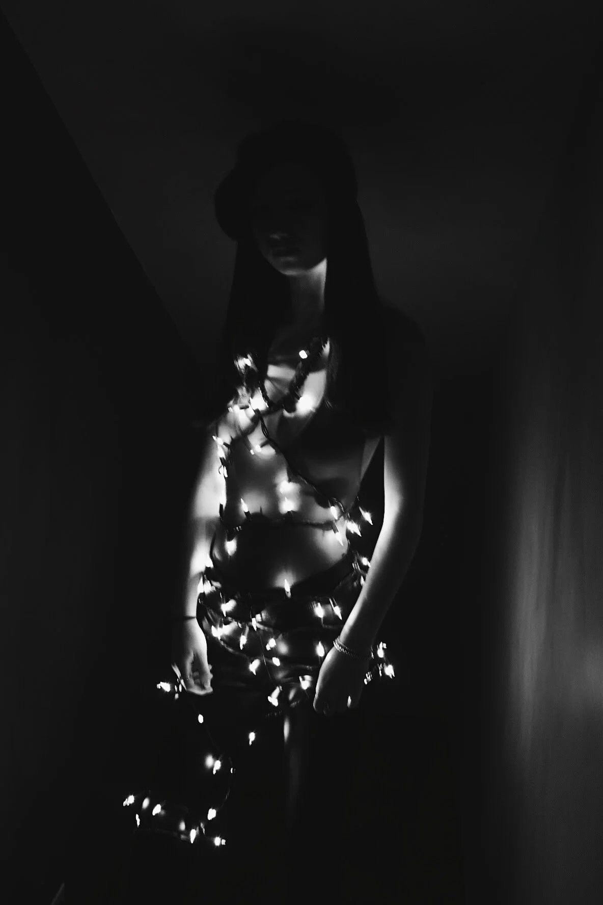 A woman wrapped in string lights, illuminated in a dark room.