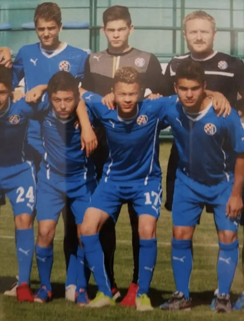 Group of young male soccer players posing on the field, wearing blue and black soccer uniforms with team logos.