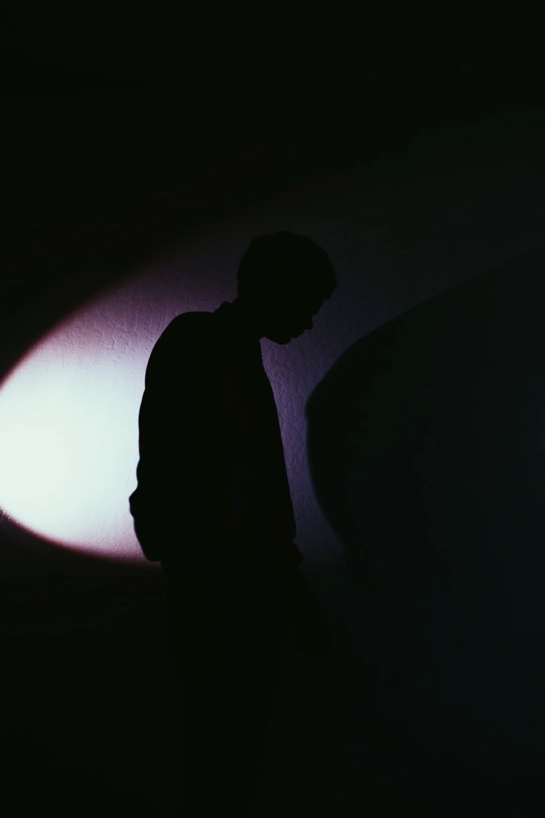 Silhouette of a person walking in front of a wall illuminated by a purple and white crescent-shaped light.
