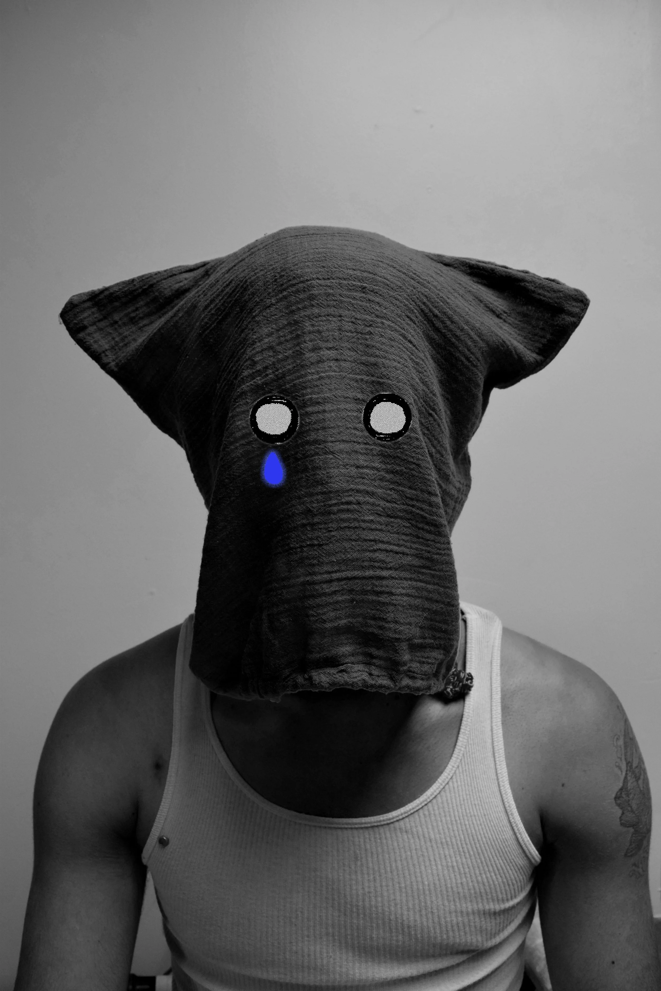 Person wearing a mask that looks like an elephant's face with sad eyes and a teardrop, in black and white, wearing a tank top.