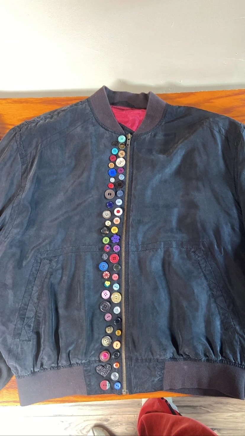 Black bomber jacket with a colorful array of buttons along the zipper.