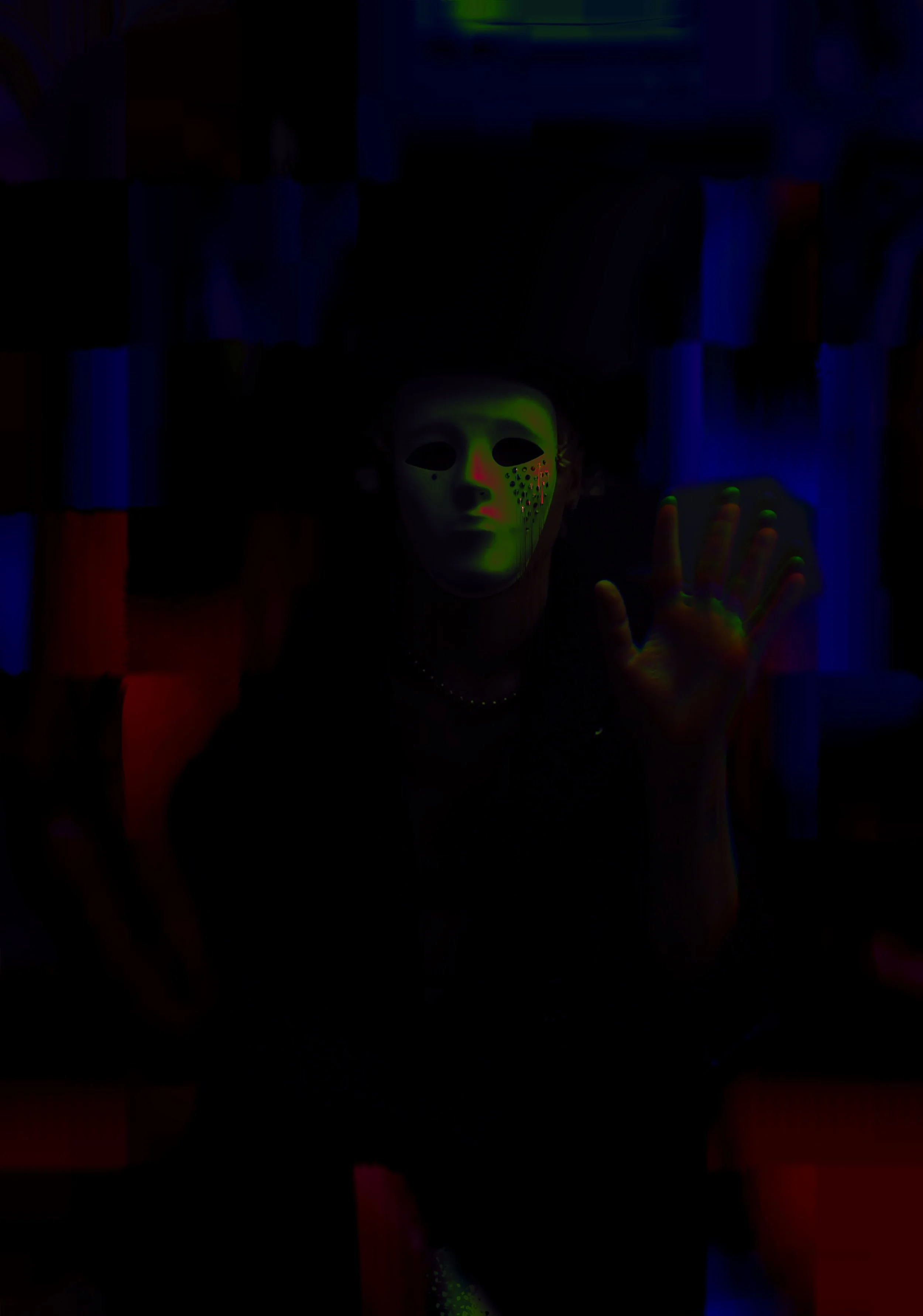 a person wearing a white mask with black eyes, a red nose, and black dots on one cheek, raising their hand in a dark, colorful room.