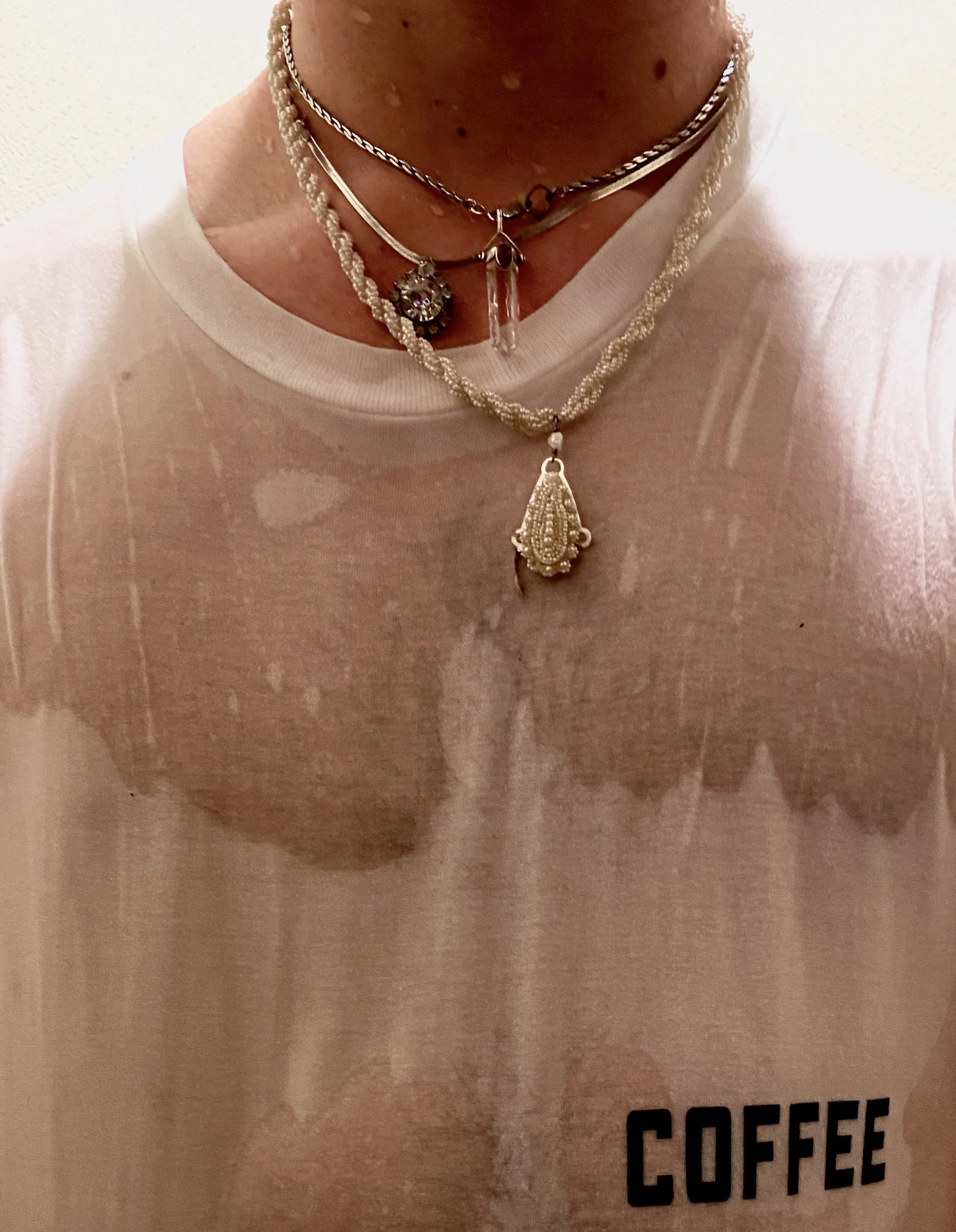 Person wearing layered silver and pearl necklaces, a clear quartz pendant, and a pink t-shirt with the word 'COFFEE' printed on it.