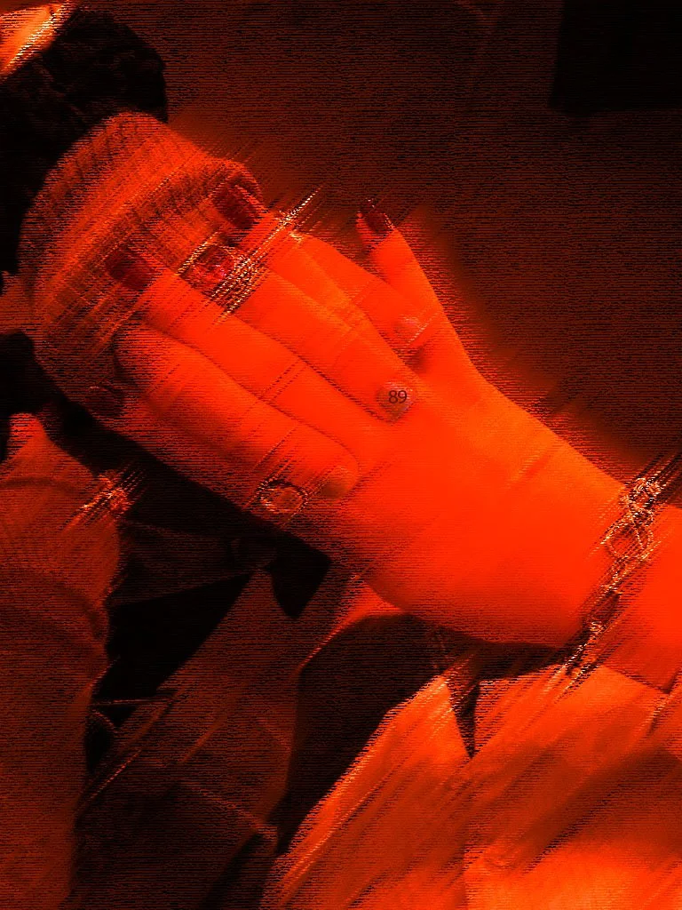 A person in a red shirt and chain is taking a selfie in front of a mirror, with a dark background.