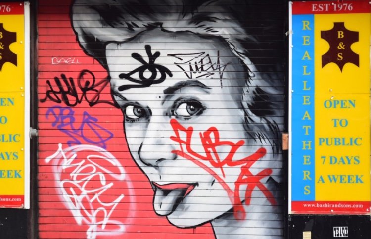 Graffiti art of a woman's face with her tongue sticking out, on a red background with colorful tags surrounding her.