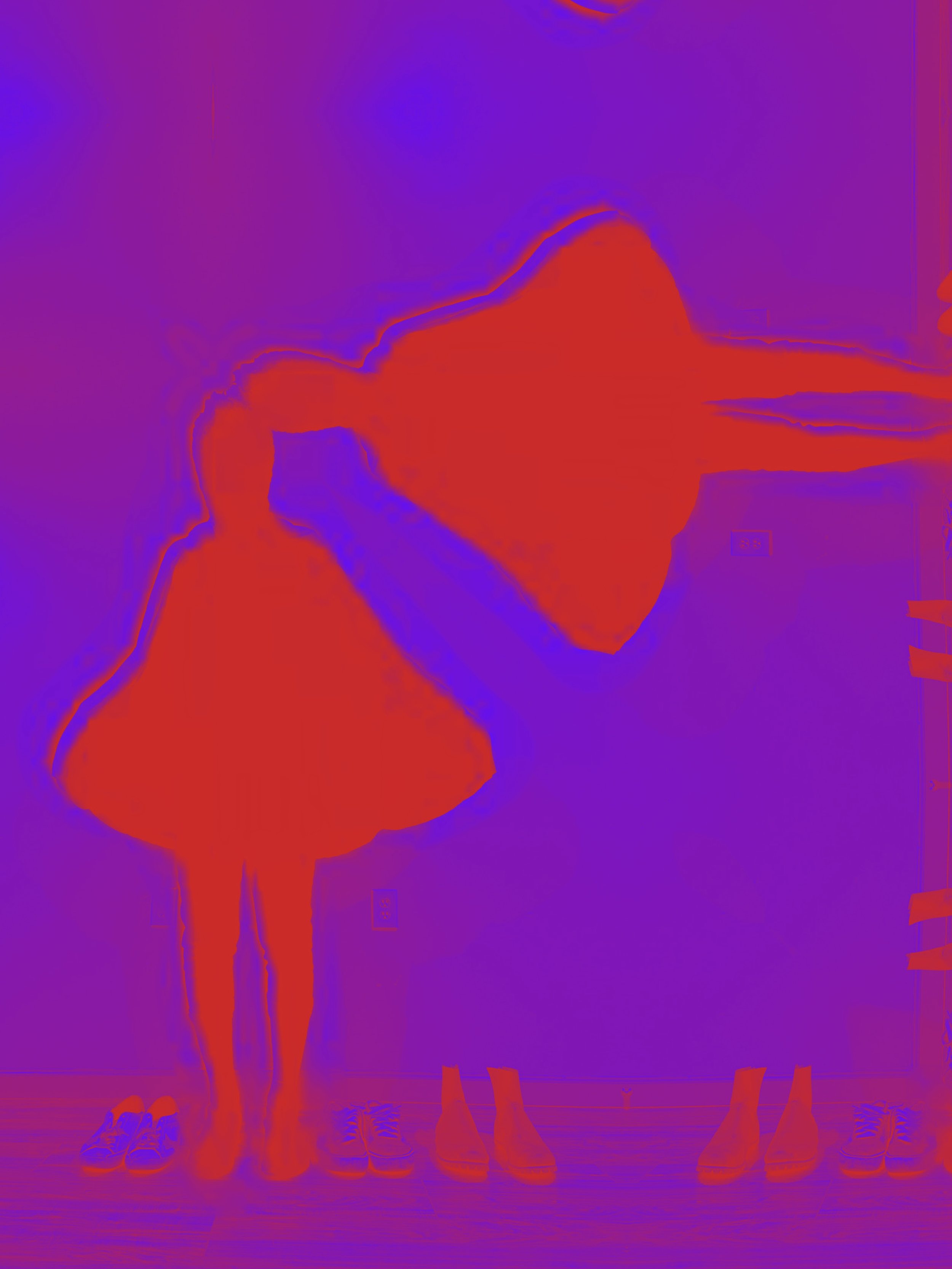 Two children in red dresses and leggings, standing and holding hands, surrounded by shoes on the floor, with a purple background.