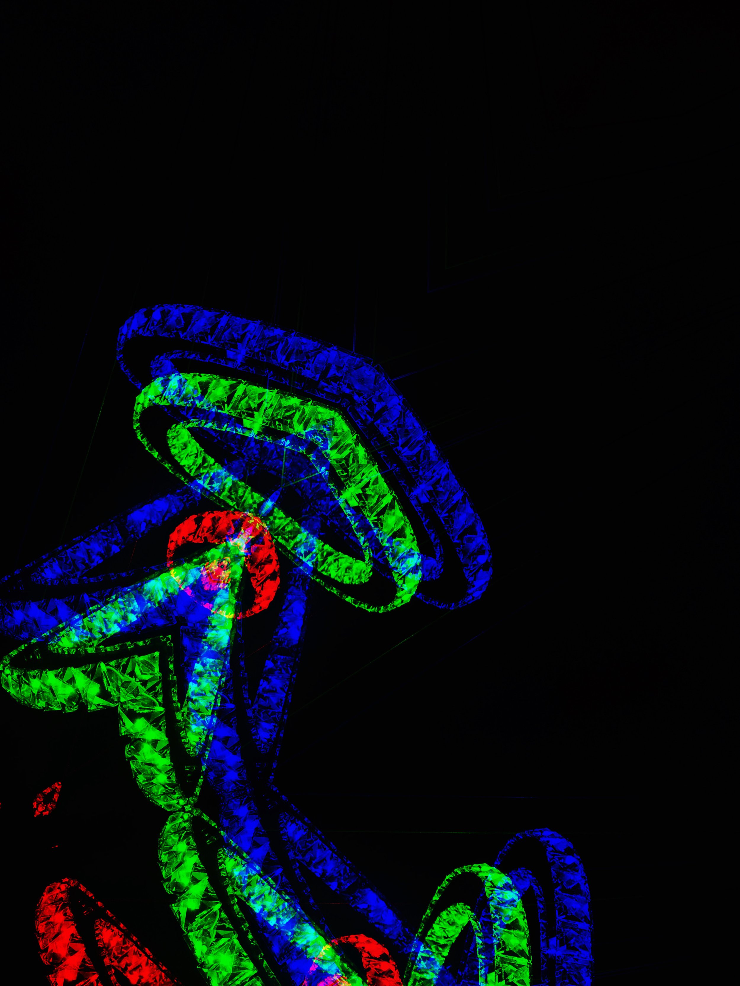 Brightly colored neon spiral light sculpture in blue, green, and red against a black background.