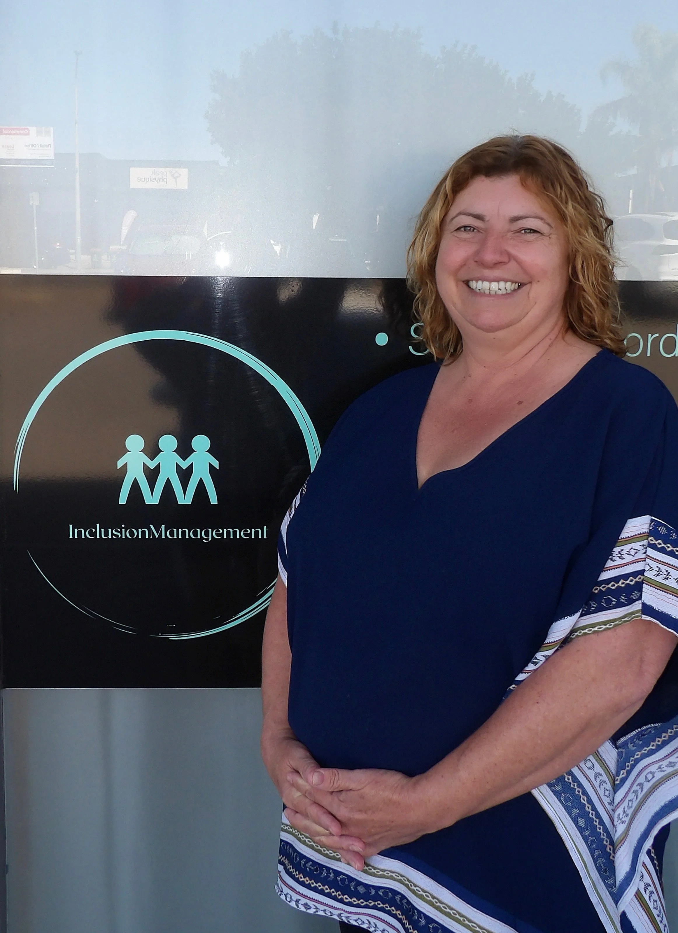 Smiling woman standing next to an inclusion and management poster with a green background.