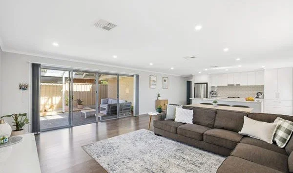 Modern living room with wooden flooring, a kitchen island, dishwasher, wooden dining table with chairs, blue recliners, and a flat-screen TV.