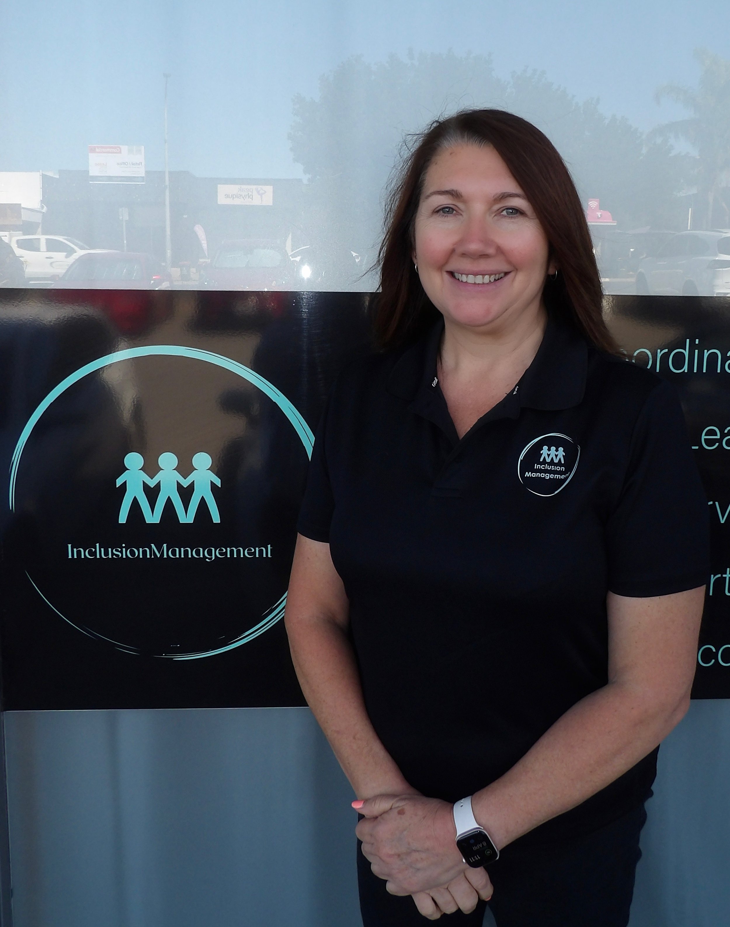 Smiling woman standing next to a banner with text mentioning "Inclusion Management" and "NDIS" against a green wall with motivational words.