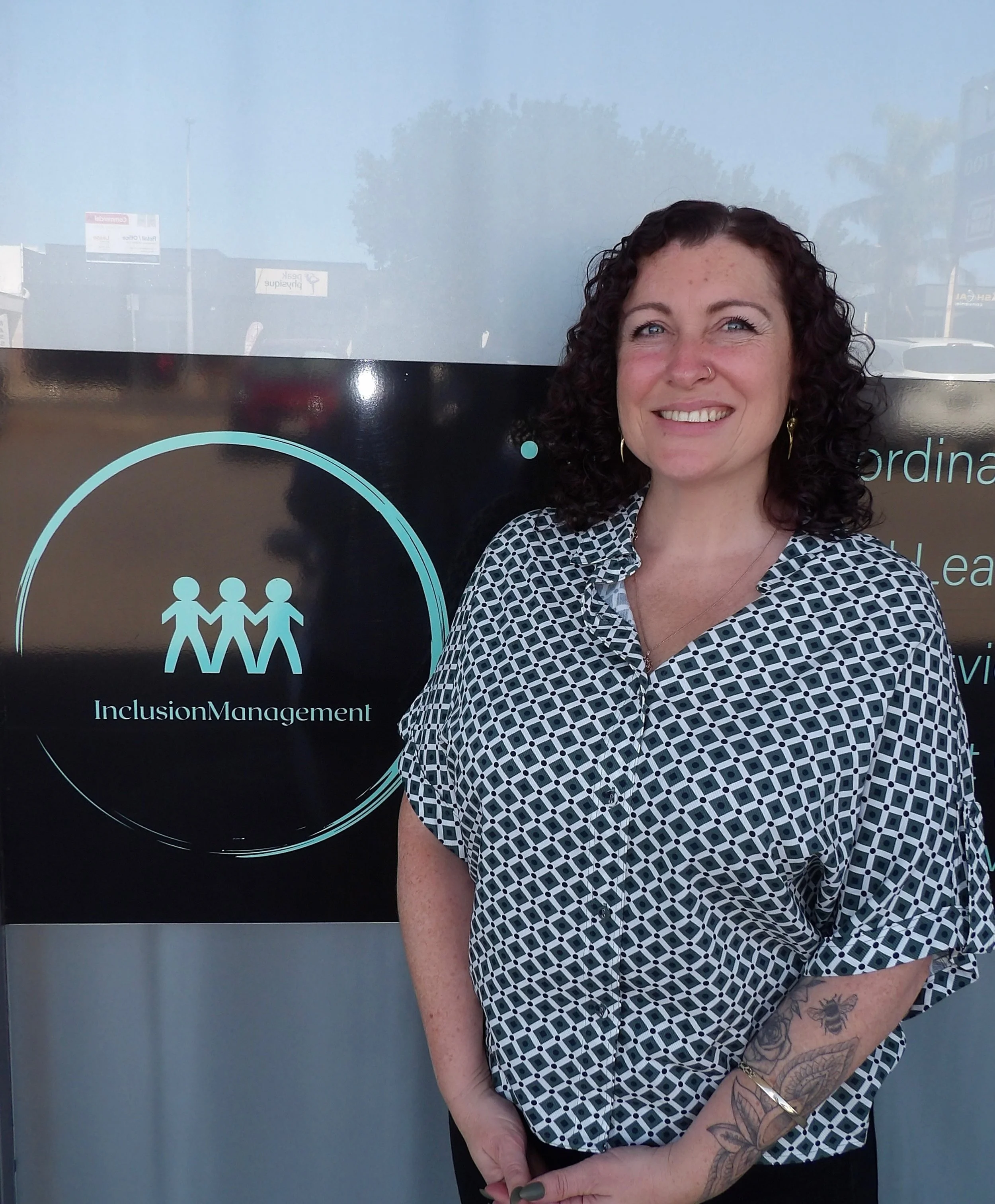Two women sitting at a table discussing a document in an office setting with a sign for NDIS Support Services in the background.