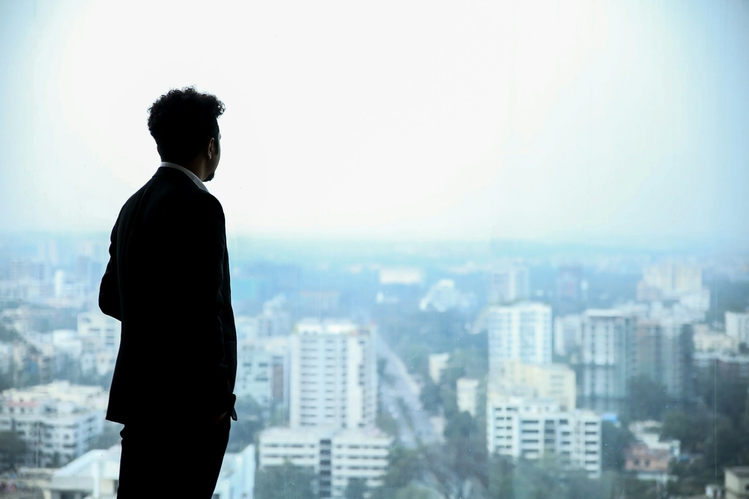 Silhouette of a man in a suit looking out over a city skyline through a large window.