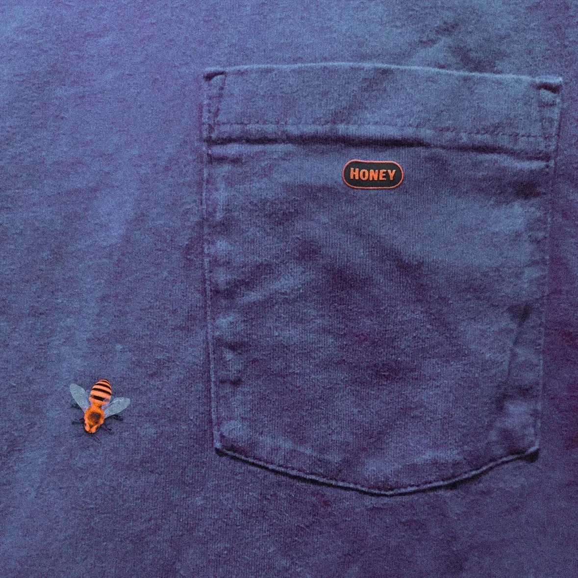 Close-up of a dark blue jean fabric with a small bee sticker and a back pocket with a small orange label that says 'HONEY', by Jalen Jordan