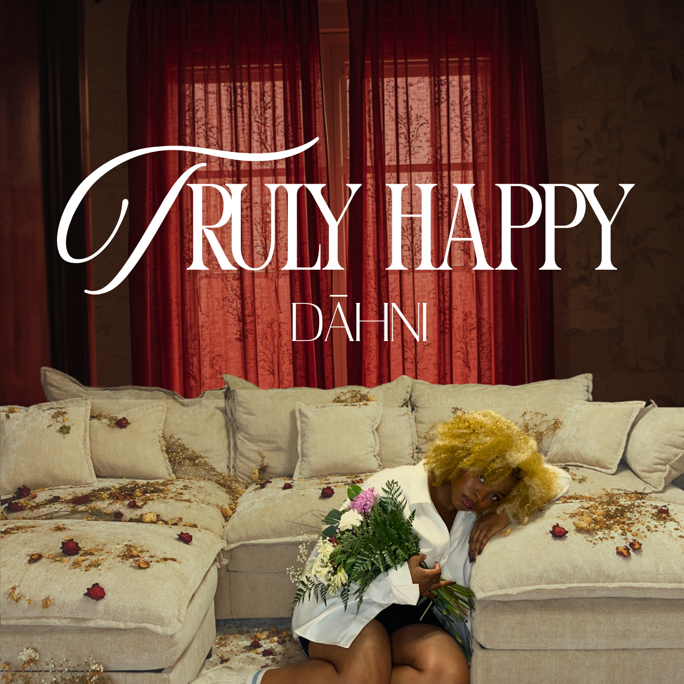  DĀHNI with curly blonde hair, sitting on a floral sofa in a room with red curtains, holding a bouquet of flowers, surrounded by scattered flower petals, with the text TRULY HAPPY cover art