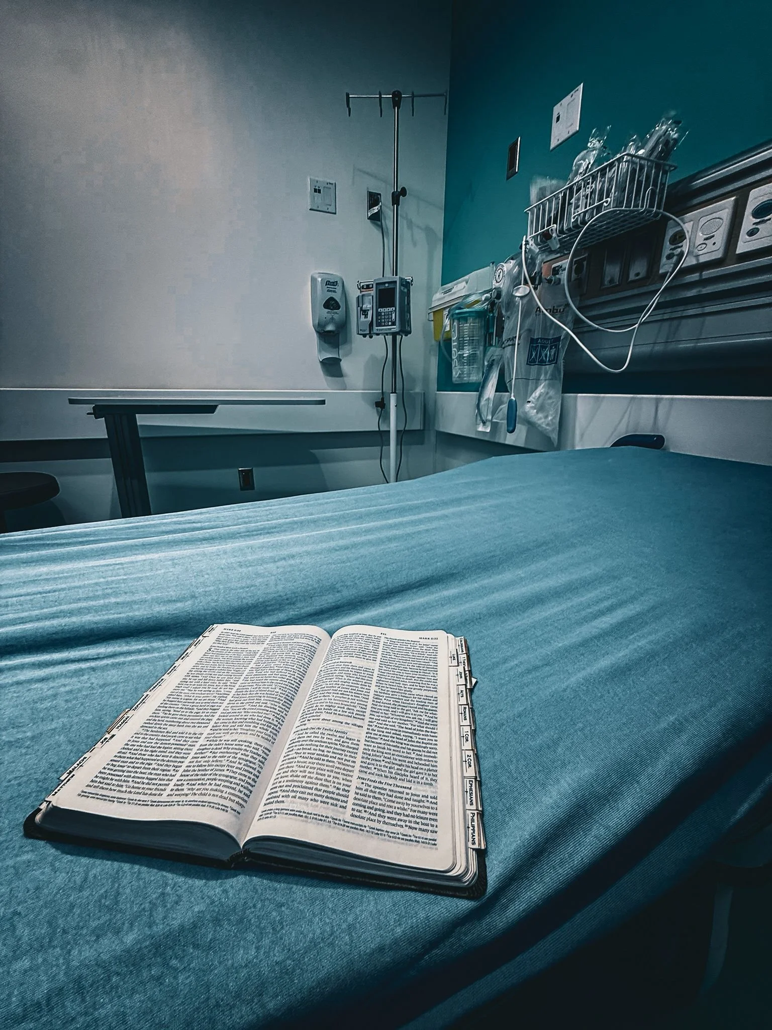 Empty hospital room with an open Bible on a hospital bed, medical equipment on the wall, and sterile surroundings. Kojo Dave After Amen Cover Art