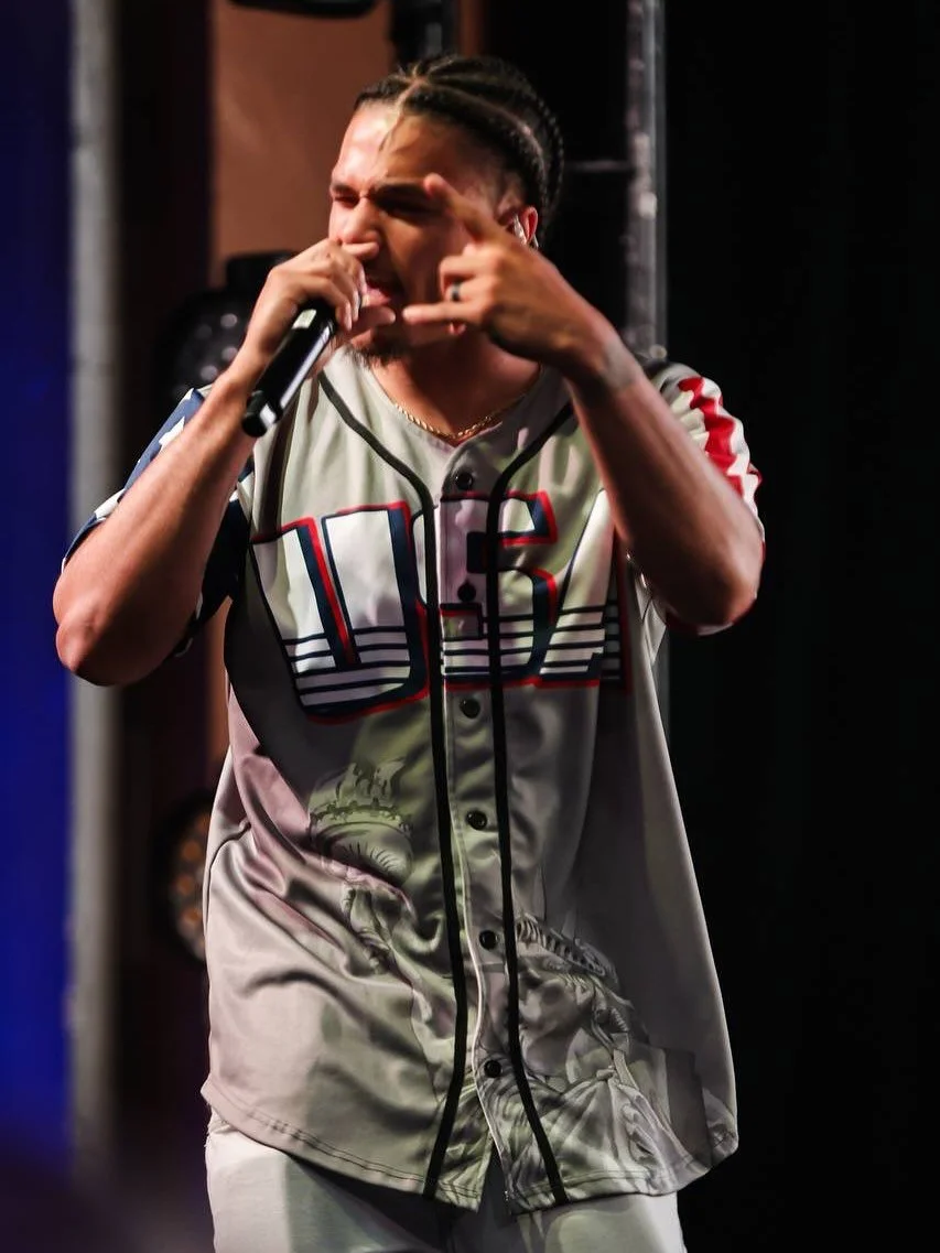 Deyton Jackson with braids rapping into a microphone on stage, wearing a baseball jersey with the number 16.