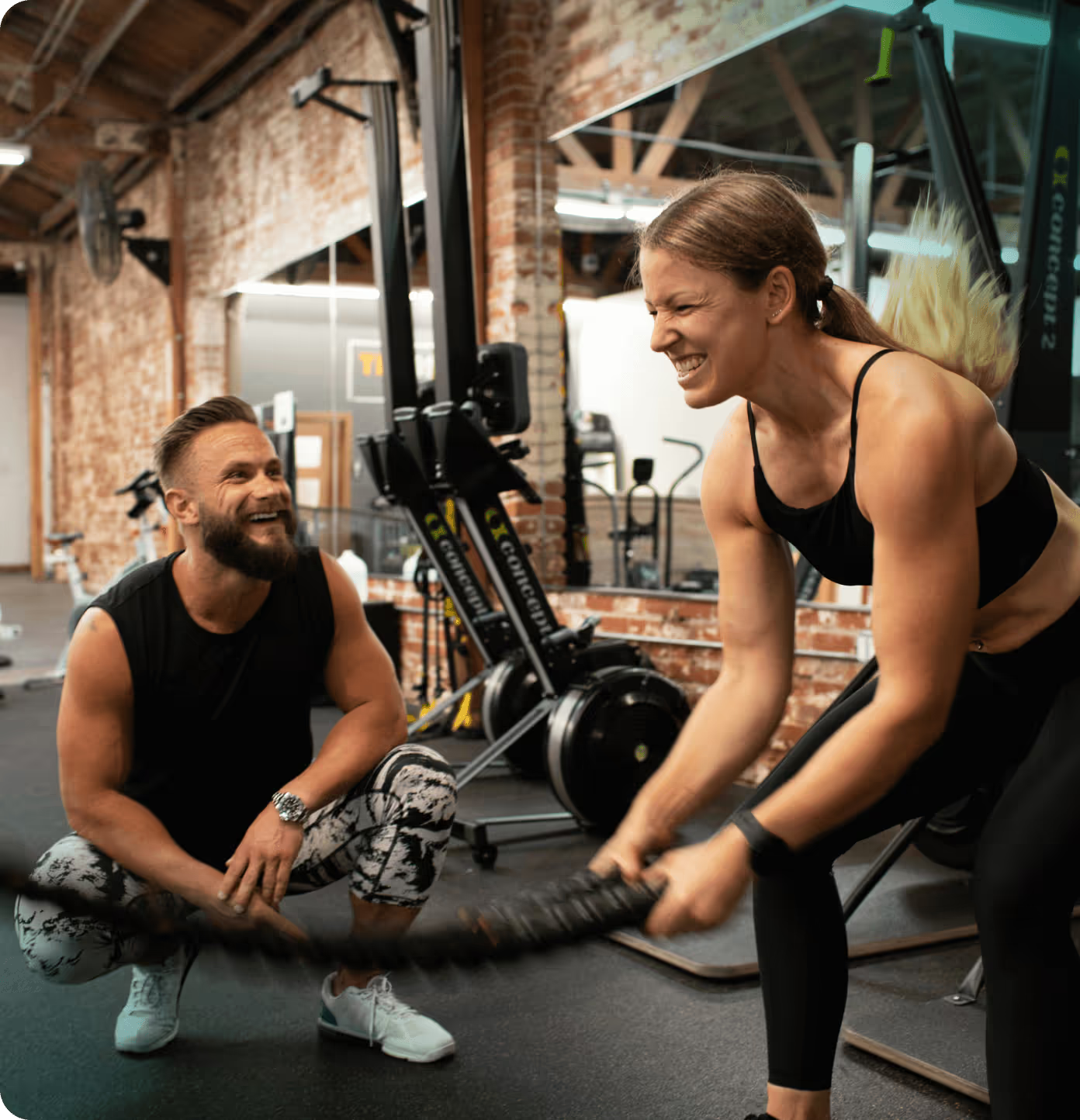 Woman exercising with battle ropes while trainer watches in gym.