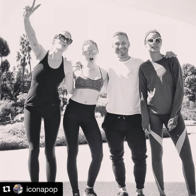 Four people posing together outdoors in athletic clothing, smiling and relaxed, with trees in the background.
