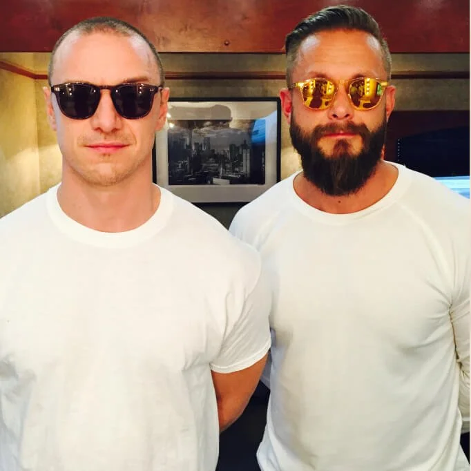 Two men wearing sunglasses and white T-shirts standing indoors.